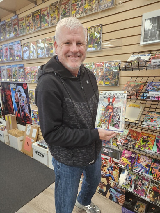 L.I. Comic Shop co-owner Jim Michalak with a copy of The Overstreet Guide To Grading Comics – Seventh Edition